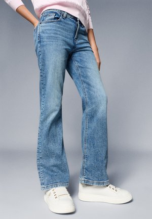 Lichtblauwe flared jeans van denim, met een hoge taille, subtiele stikdetails en versleten randen, gecombineerd met witte sneakers.