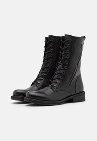 Bottes de combat en cuir noir avec un design à lacets, œillets métalliques, fermeture éclair latérale et semelle en caoutchouc texturée.