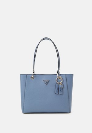 Niebieska skórzana torba typu tote z podwójnymi uchwytami, trójkątnym logo Guess i wiszącymi brelokami oznaczonymi "Guess" i "1981".