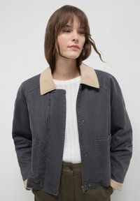 Giacca con collare in grigio scuro con colletto in corduroy beige. Presenta chiusure a scatto, tasche laterali e una vestibilità rilassata. Dettaglio in tessuto testurizzato.