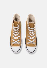 Wysokie sneakersy w musztardowo-żółtym kanwasie z białymi sznurówkami, białą gumową osłoną palców i czarnymi detalami na podeszwie. Klasyczny design z przeszyciami.