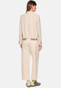 Beige jacket with elastic hem and long sleeves paired with loose beige pants featuring a black and white striped waistband.