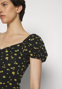Top de tecido preto com mangas curtas bufantes, apresentando um padrão de flores amarelas. O decote é quadrado, com detalhes de costura franzida.