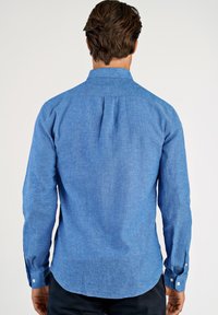 Camicia a maniche lunghe azzurro chiaro con una trama sottile, colletto a punta e polsini chiusi con bottoni bianchi. Tessuto liscio, vestibilità aderente.