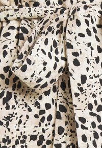 Tissu beige avec un motif léopard noir, présentant un détail de nœud noué et une surface douce et texturée.