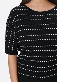 Haut en tricot noir avec des rayures horizontales blanches et des motifs ouvragés. Manches courtes avec des poignets côtelés, col rond et détail texturé.