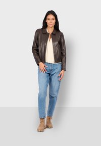 Veste en cuir marron avec un col et des poches avant, associée à un jean en denim bleu clair et des bottes à lacets beiges.