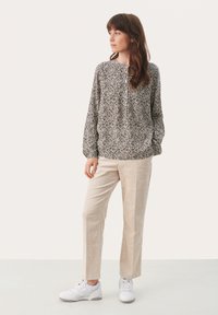 Zwart-wit bloeiende blouse met lange mouwen, gecombineerd met beige corduroy broek en witte sneakers; ontspannen pasvorm met een ronde halslijn.