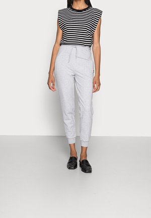 Schwarz-weiß gestreiftes ärmelloses Top, kombiniert mit grauen Sweatpants mit elastischem Bund und Knöchelabschlüssen. Schwarze Slipper.