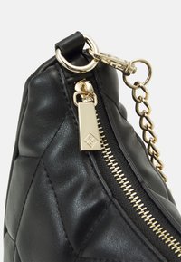 Sort quilted læder håndtaske med guldhardware, lynlås lukning og kæde accent. Teksturen er glat med synlig syning.