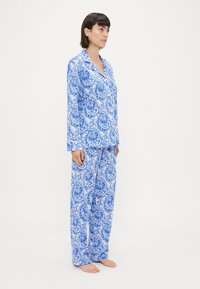 Kék és fehér mintás pizsama szett virágos és paisley mintákkal. Hosszú ujjú felső és bő szabású nadrág. Puha szövet textúra.