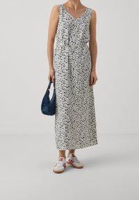Maxi-jurk met luipaardprint in gebroken wit, met een V-hals, een cinched taille met een strik. Gecombineerd met een blauwe tas en witte sneakers met rode accenten.