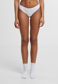 Witte katoenen onderbroeken hebben een laag uitgesneden snit en een gladde textuur. Gecombineerd met witte franje enkelsokken, gepresenteerd tegen een neutrale achtergrond.