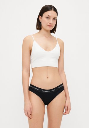 Fehér bralette v-nyakú dizájnnal és vékony pántokkal, fekete bikini bugyival, amelynek márkás derékrésze van. Sima szövet textúra.