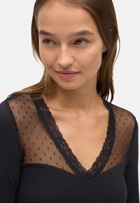 Camiseta negra de manga larga con un escote de malla transparente con puntos y un ribete de encaje que crea un diseño en forma de V. Textura de tela suave.