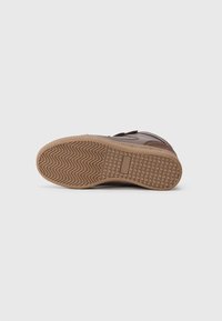 Braune Sneaker mit einer strukturierten Gummisohle, die ein Zickzackmuster aufweist. Der obere Teil besteht aus verschiedenen Brauntönen und glatten Texturen.
