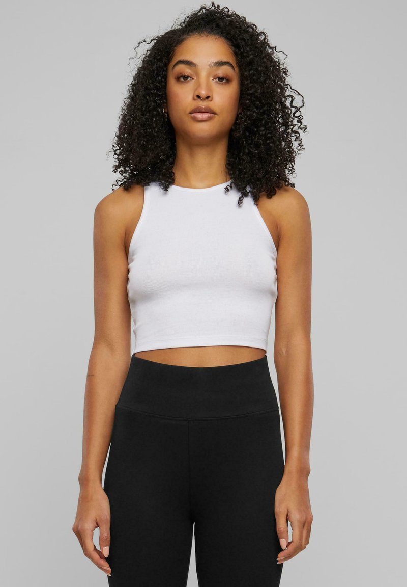 Witte geknipte tanktop met een hoge hals en slanke pasvorm, gecombineerd met hoge zwarte leggings; gladde stof en minimalistisch ontwerp.