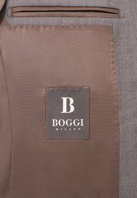 Szara materiałowa podszewka kurtki z brązową metką z logo "BOGGI MILANO" i dużą literą "B". Gładka faktura, staranne szwy.