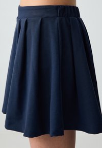 Marineblauer, plissierter Rock aus weichem Stoff, mit einem elastischen Bund und einer ausgestellten Silhouette. Der Saum liegt über dem Knie.