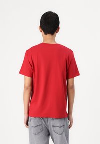 Camiseta de algodón roja con mangas cortas, escote redondo y corte relajado. Combinada con jeans de mezclilla gris, mostrando vista trasera.