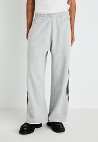 Gray sweatpants made of soft fabric, featuring a loose fit, elastic waistband, side pockets, and a black graphic design on one leg.