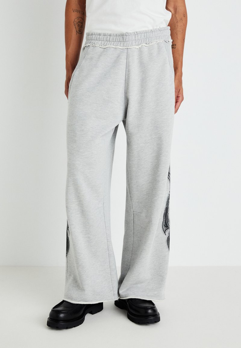 Gray sweatpants made of soft fabric, featuring a loose fit, elastic waistband, side pockets, and a black graphic design on one leg.