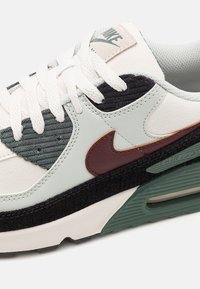 Vita och gröna sneakers med texturerad tyg och läderdetaljer, som har en brun Nike-logotyp och en svart mellansula, designad för komfort.