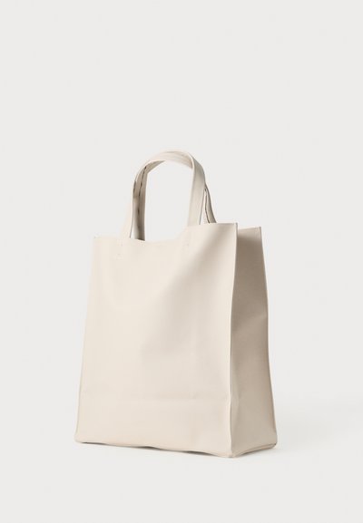 Beige színű, strukturált formájú tote táska, sima anyagból készült. Két rövid fogantyúval rendelkezik, és látható varrások futnak az élek mentén.