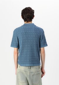 Short-sleeve polo shirt in textured blue fabric with a zigzag pattern and a collar. Features a straight hem and ribbed cuffs.