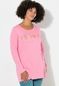 Pitkähihainen vaaleanpunainen paita, jossa on monivärinen brodeerattu teksti "OLE ONNELLINEN" rinnassa. Pehmeä kangas, joka on rento istuimaltaan.