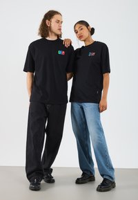 Black cotton t-shirts with colorful graphic patches, relaxed fit. Pairing with dark and light denim pants and sturdy black footwear.