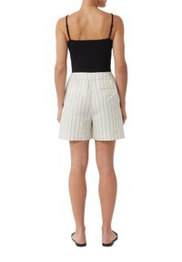 Leichte cremefarbene Shorts mit schwarzen vertikalen Streifen, ausgestattet mit hoher Taille, Gesäßtaschen und einem bequemen Schnitt. Kombiniert mit einem schwarzen Tanktop.