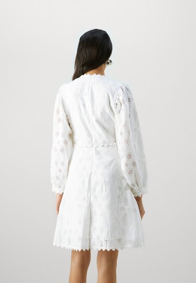 Robe blanche avec broderie florale et manches longues transparentes. Ourlet festonné et tissu texturé avec une taille ajustée. Vue arrière montrée.