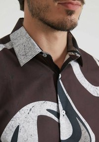 Chemise brune à motifs avec un col en pierre léger gris clair et des motifs abstraits blancs, dotée d'une fermeture à boutons et d'une texture de tissu lisse.