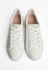 Sneakers bianchi con lacci, dotati di una soffice fodera interna rosa e di un marchio discreto. Lo sfondo è bianco semplice, che evidenzia le scarpe.
