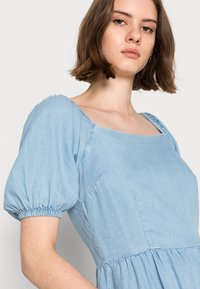 Vestido de denim texturizado azul claro com decote quadrado e mangas curtas bufantes com punhos elásticos e uma cintura ajustada.