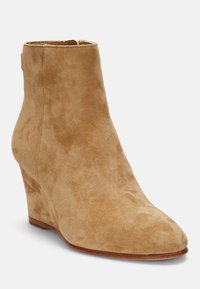 Stivale alla caviglia in suede beige con tacco a cuneo, punta affusolata e finitura liscia. Presenta una scarpetta corta e dettagli di cucitura sottili.