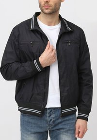 Veste bomber en nylon noir avec poches zipp ées sur la poitrine, poignets côtelés avec des rayures grises et col montant.