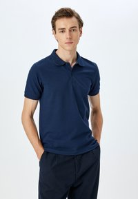 Marineblå pikétröja gjord av mjuk bomull, med en tvåknappslåda, korta ärmar och texturerad krage. Slät, klassisk passform.