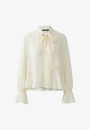 Cream-colored long-sleeve blouse with a large bow tie at the neck, flared cuffs, and a slight peplum hem.