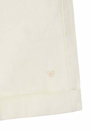 Primer plano de tela color crema con un pequeño y sutil logo bordado de una raqueta de tenis cerca del dobladillo y con costuras visibles.