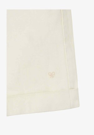 Primer plano de tela color crema con un pequeño y sutil logo bordado de una raqueta de tenis cerca del dobladillo y con costuras visibles.