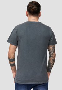 Grijze katoenen t-shirt met ronde hals, korte mouwen en een licht versleten afwerking. Zichtbare tatoeages op de armen. Eenvoudige achterkant.