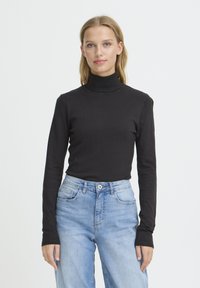 Haut à col roulé noir en matière douce et extensible avec manches longues, associé à un jean taille haute bleu clair. Design simple et minimaliste.