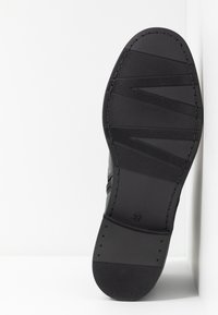 Semelle de chaussure en caoutchouc noir avec une accroche texturée, comprenant des bandes horizontales et un talon arrondi. La taille 37 est embossée sur le dessous.