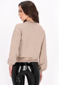 Maglione beige con maniche a sbuffo, decorato con piccole perle bianche, polsini e orlo a coste, abbinato a leggings neri lucidi.