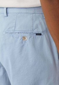 Pantaloni azzurri con una texture liscia, dotati di tasca posteriore, chiusura con bottone e un'etichetta del marchio cucita sulla tasca.