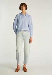 Lichtblauw gestreept overhemd met knopen en een kraag, gecombineerd met vervaagde lichtblauwe spijkerbroek en bruine loafers met een gouden accent.