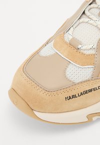 Sneaker bej cu panouri din suede și plasă, detalii cusute, un logo pe lateral, șireturi și guler căptușit.
