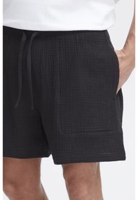 Black cotton shorts with a textured, crinkled design, featuring an elastic waistband and side pockets.